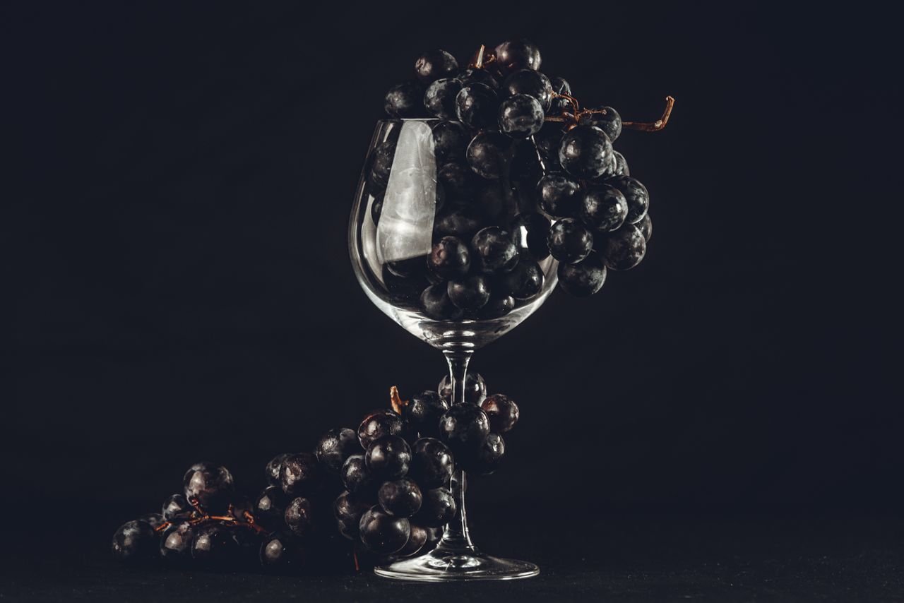 our-story-02 A dramatic composition featuring black grapes artfully arranged in a wine glass.