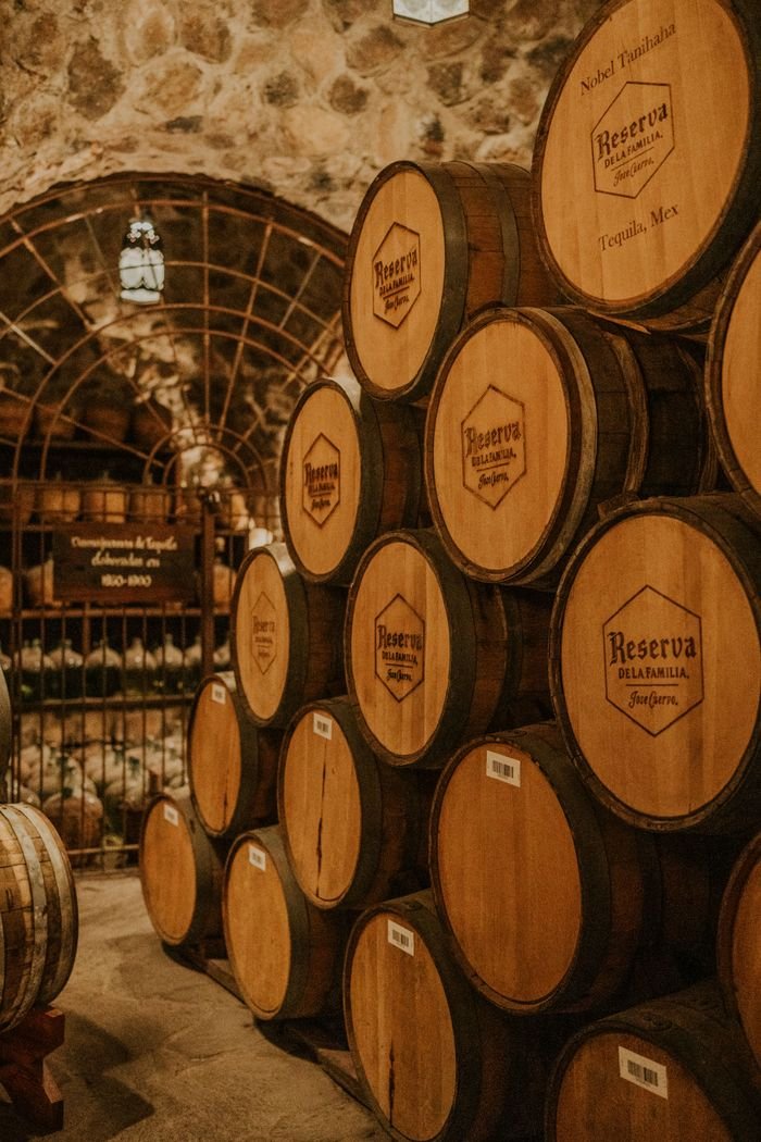 Stacked wooden tequila barrels aging in a Mexican distillery cellar. Rustic atmosphere.